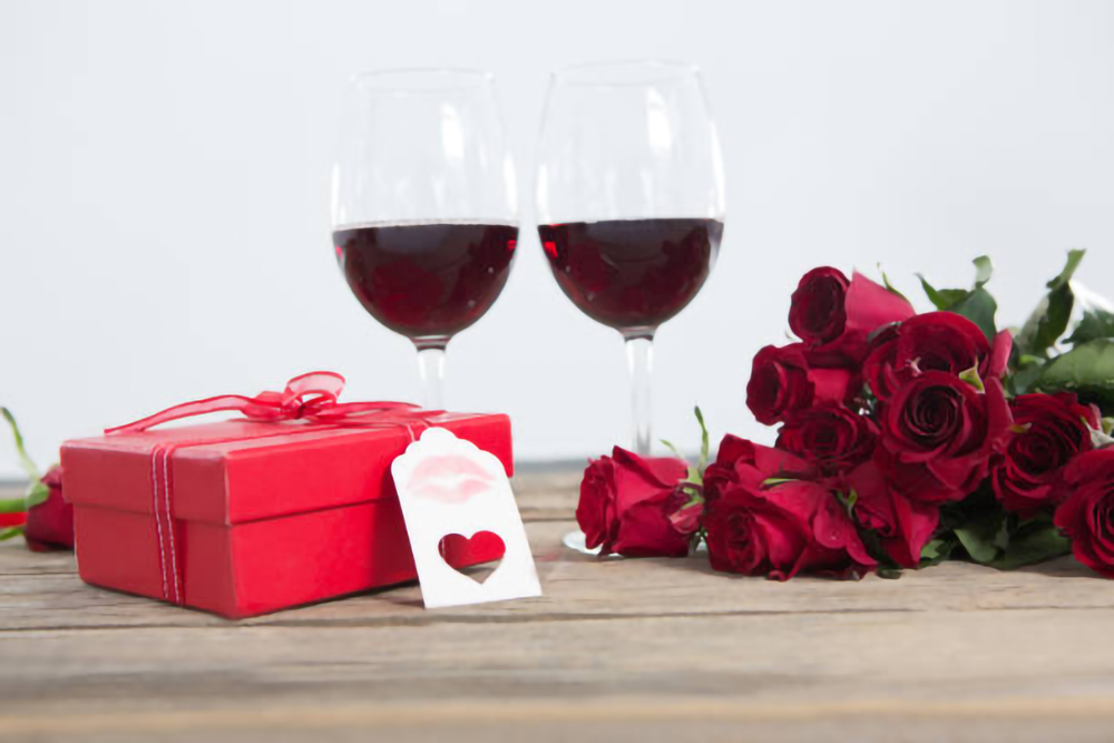 Primo piano di bicchieri di vino rosso, regalo e rose su una superficie di legno